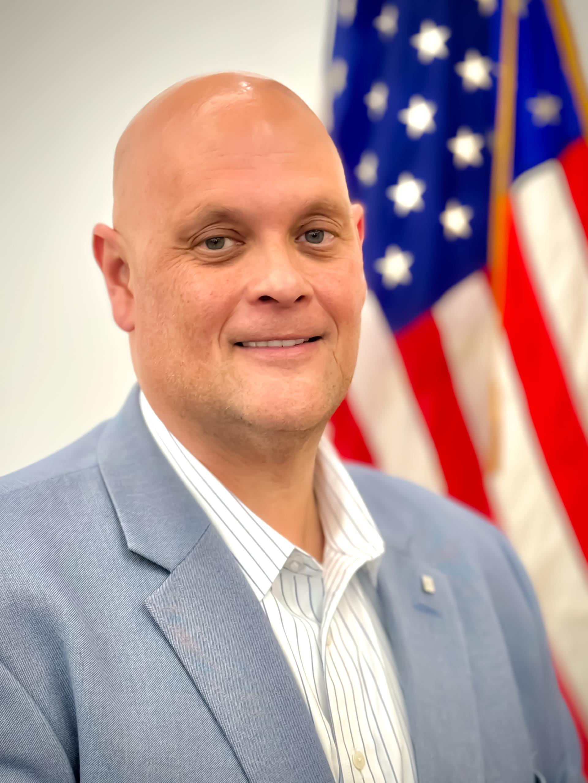 Planning Board Vice Chairman, Jason Morehouse wearing a grey suit standing in front of American flag