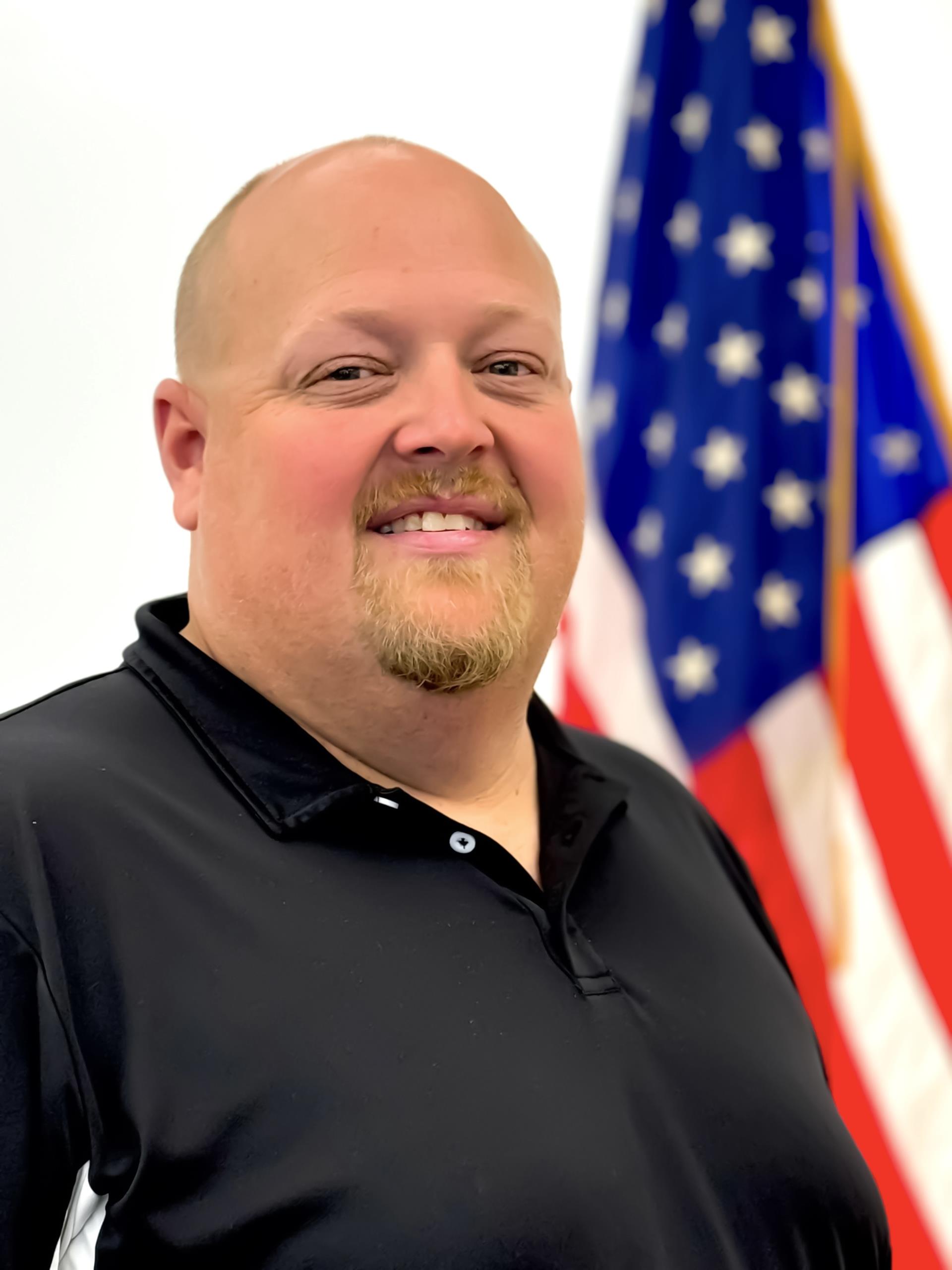 Planning Board Member, Matthew Jones wearing a black shirt standing in front of American flag